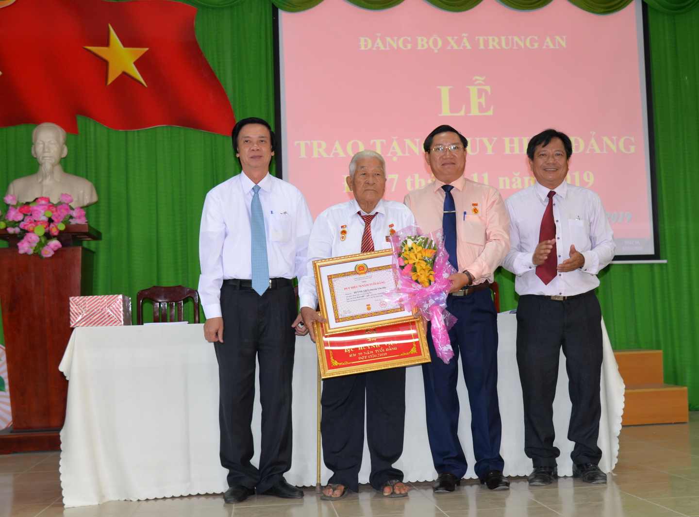 Bí thư Tỉnh ủy Nguyễn Văn Danh trao Huy hiệu 70 năm tuổi đảng và Bí thư Thành ủy Mỹ Tho, Bí thư Đảng ủy xã Trung An trao quà, hoa và khánh vàng cho đảng viên Huỳnh Việt (Huỳnh Văn Hộ).