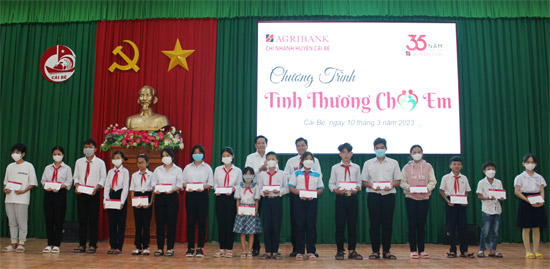 Ông Trương Văn Đoàn, Phó Giám đốc Agribank tỉnh Tiền Giang (hàng sau bên trái) và Ông Nguyễn Việt Trường, Phó Giám đốc Agribank huyện Cái Bè trao quà cho các em bị mồ côi.
