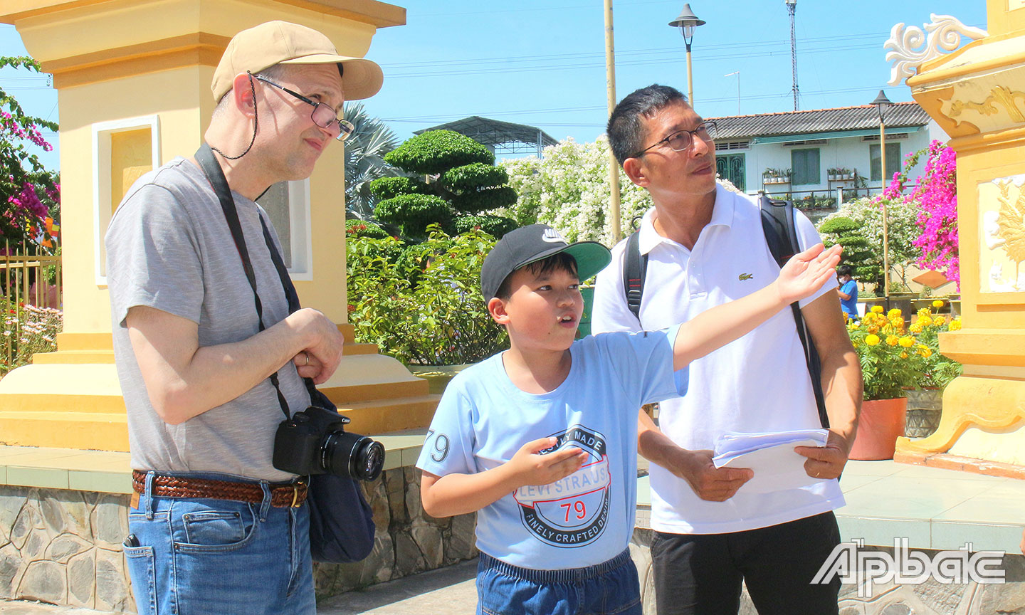  Du khách nước ngoài được hướng dẫn viên nhí giới thiệu về nét văn hóa, kiến trúc chùa Vĩnh Tràng.