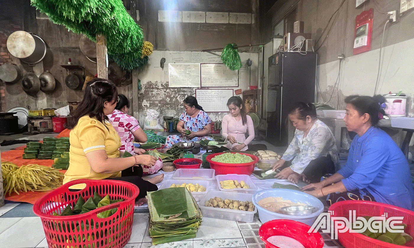 Trong nhà cả con trai, con dâu, hàng xóm đang cùng nhau xúm lại gói bánh.